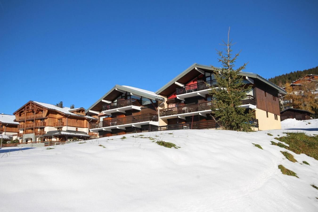 A wooden chalet-style building with multiple balconies, set against a snowy landscape with clear skies.