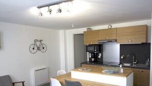 A modern kitchen with wooden cabinets, a built-in microwave, and a coffee machine. There is a dining area with a wooden table and four chairs. A bicycle is mounted on the wall.