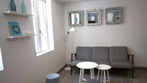 A living room with a grey sofa, two white round tables, a blue stool, a floor lamp, and three wall-mounted mirrors.
