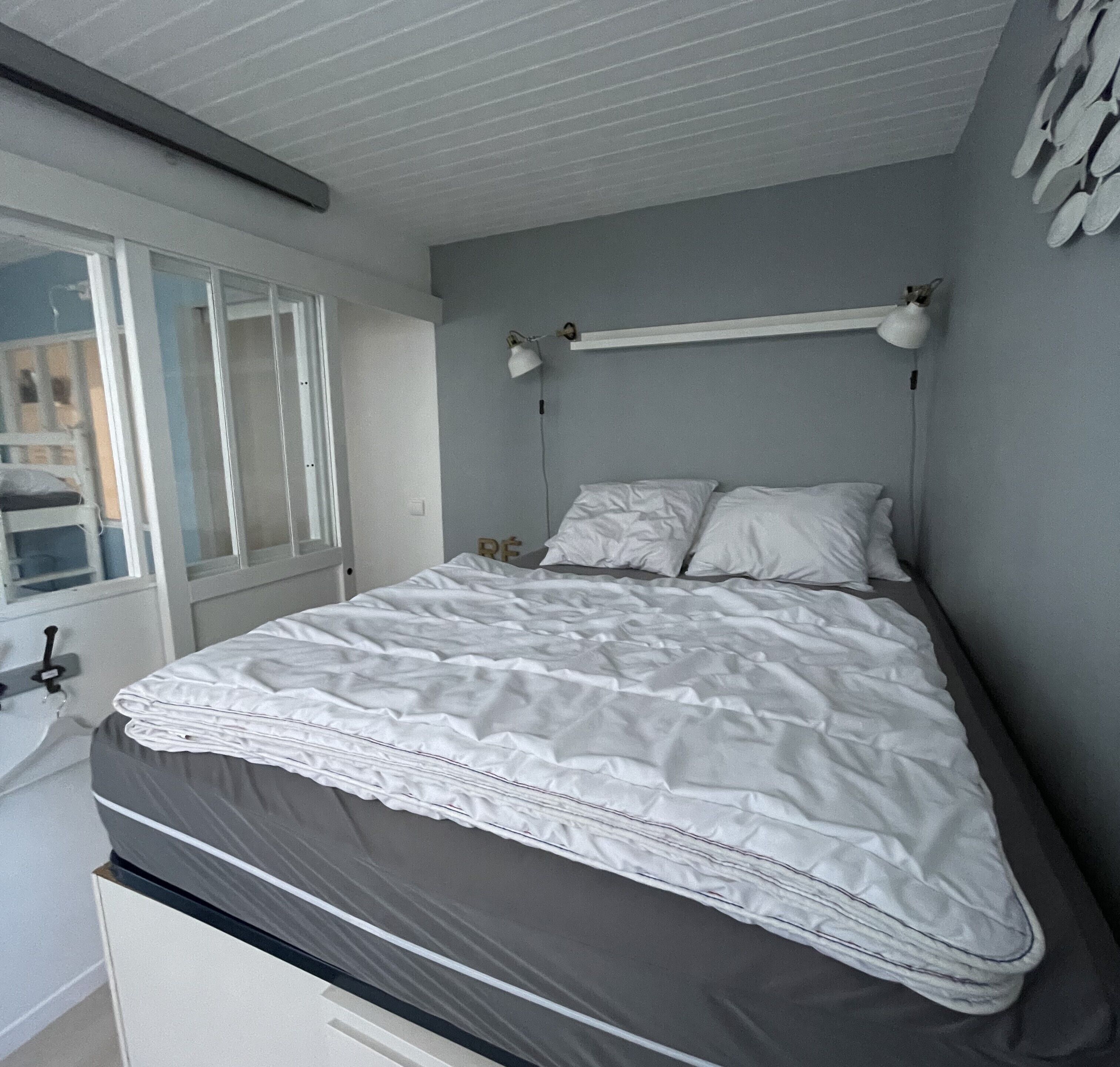A bedroom with a bed, a window, and a wall-mounted lamp.