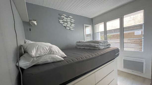 A bedroom with a bed, pillows, a wall-mounted lamp, and a window with a view of the outside.