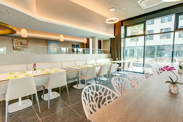 A modern dining area with white chairs, a wooden table, and a view of the outdoors through large windows.
