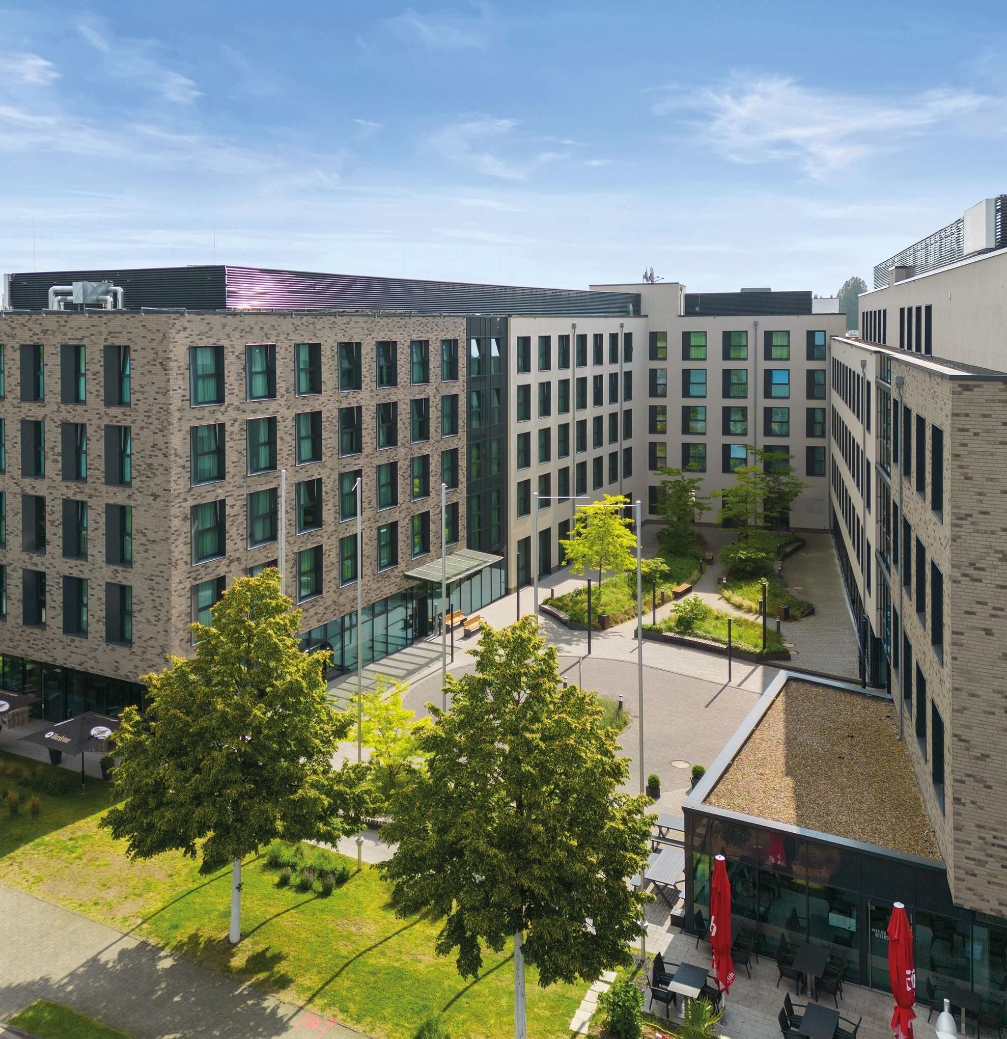 Un immeuble à plusieurs étages doté d’une cour intérieure, d’un espace extérieur aménagé pour s’asseoir et dont la façade est un mélange de briques et de verre.