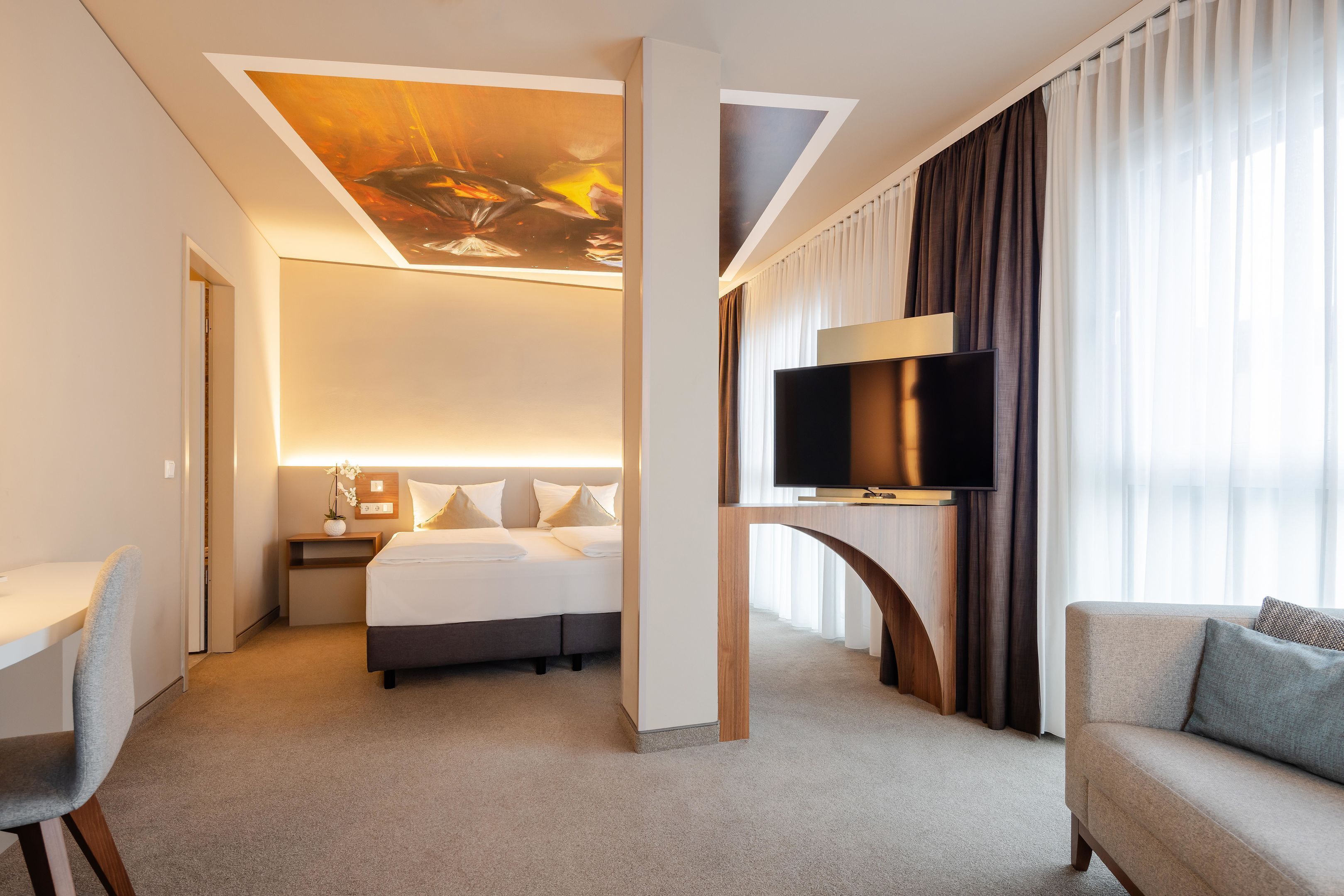 A hotel room with a bed, a desk, a TV, and a large window with curtains.