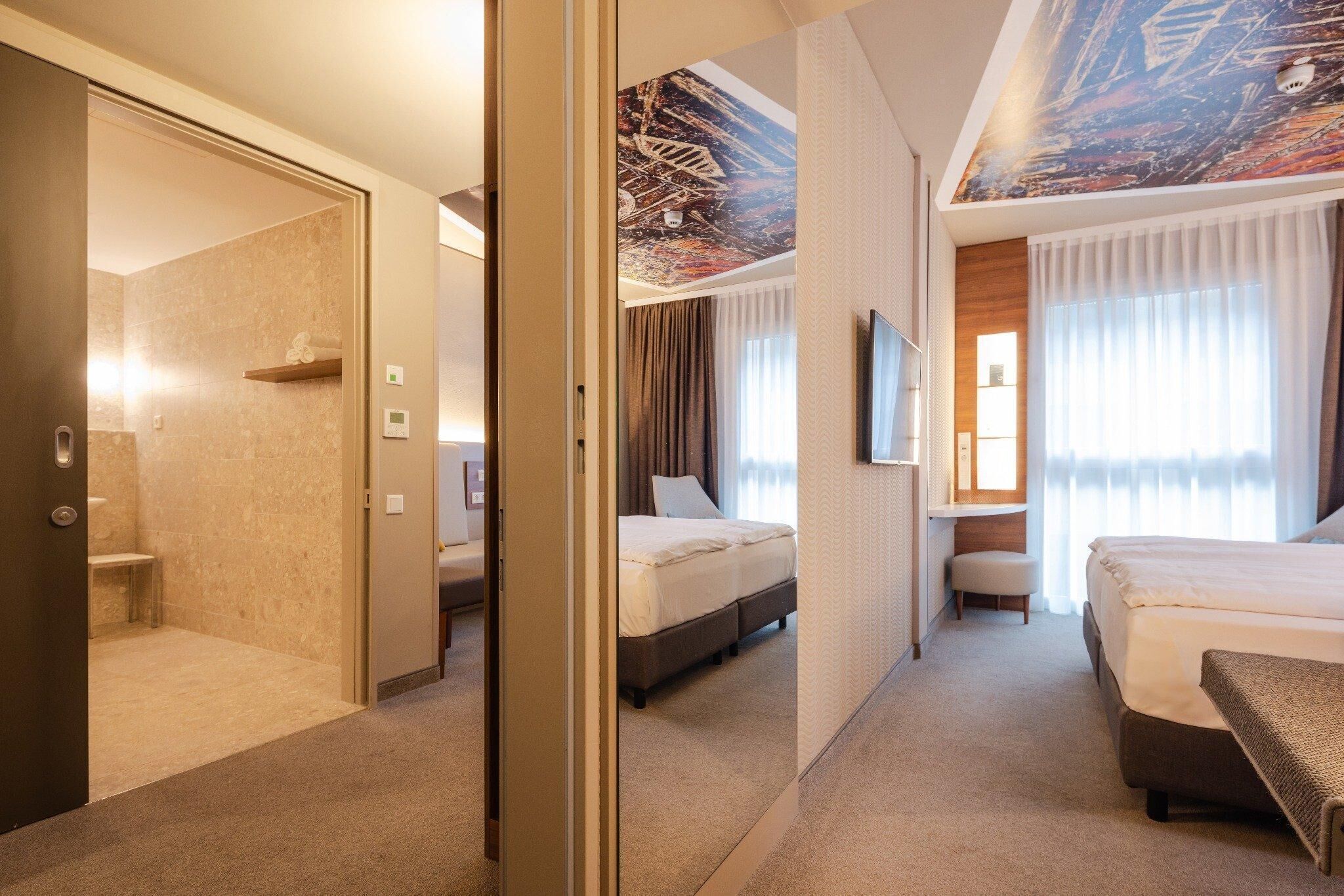 Une chambre d’hôtel avec un grand lit, un bureau, une chaise, un miroir et un espace douche.
