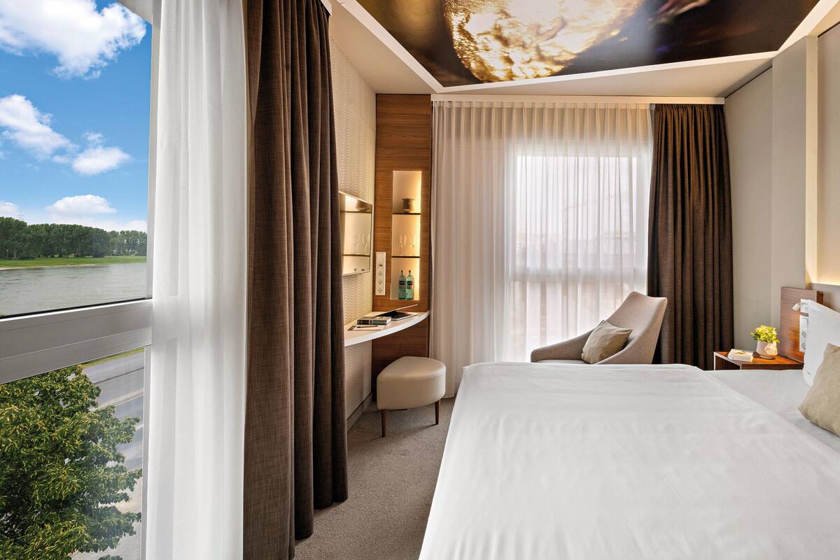 A hotel room with a bed, a desk, and a chair. There is a view of a body of water outside the window.