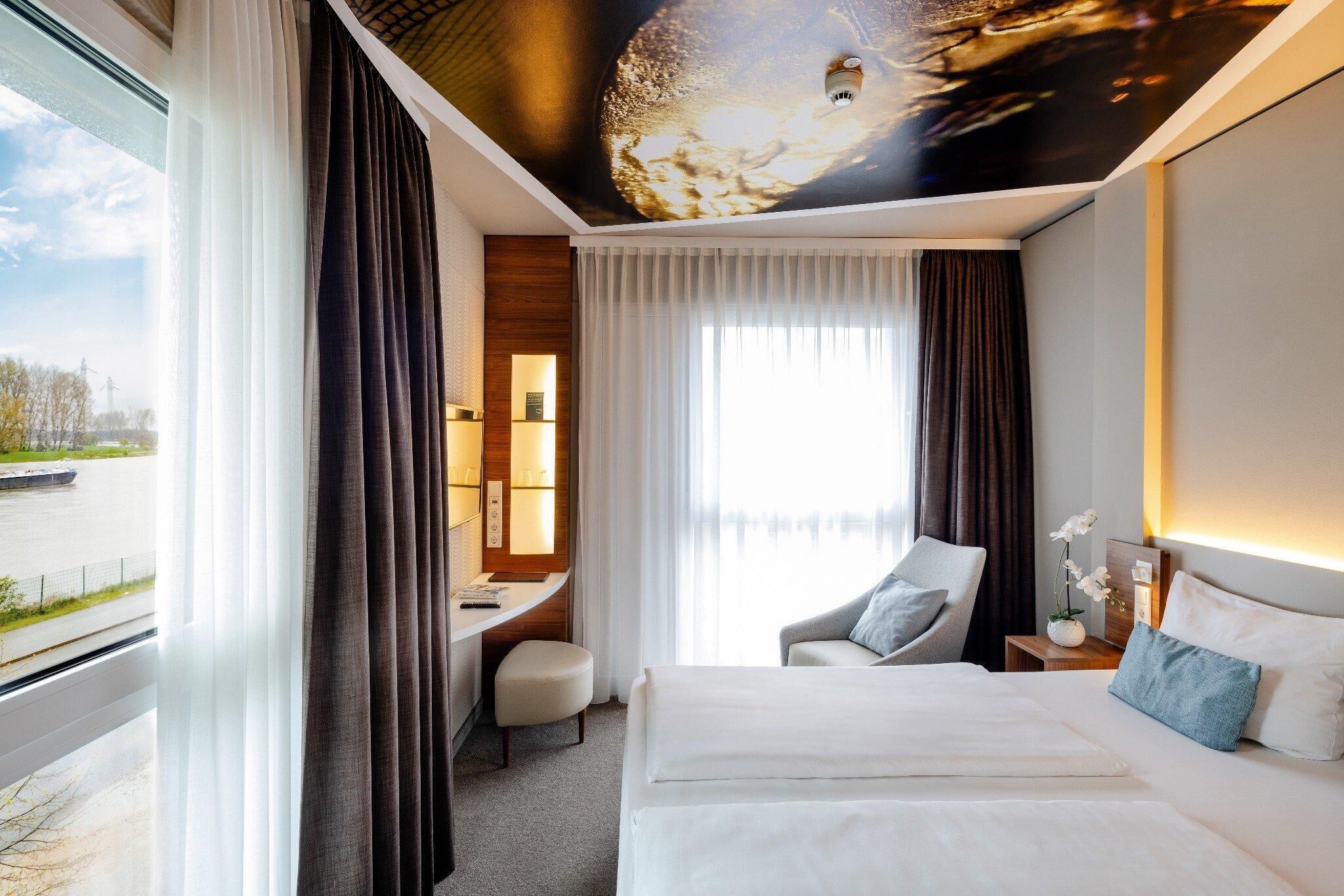 Habitación de hotel con cama, escritorio, silla y vistas al exterior.