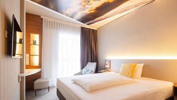 Ein Hotelzimmer mit Bett, Schreibtisch, Stuhl, Fernseher und Wandgemälde an der Decke.