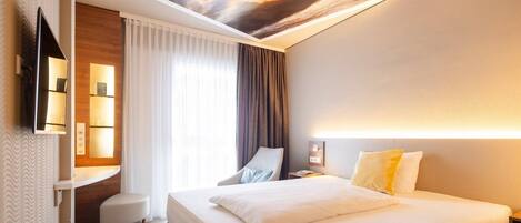 A hotel room with a bed, a desk, a chair, a TV, and a ceiling mural.
