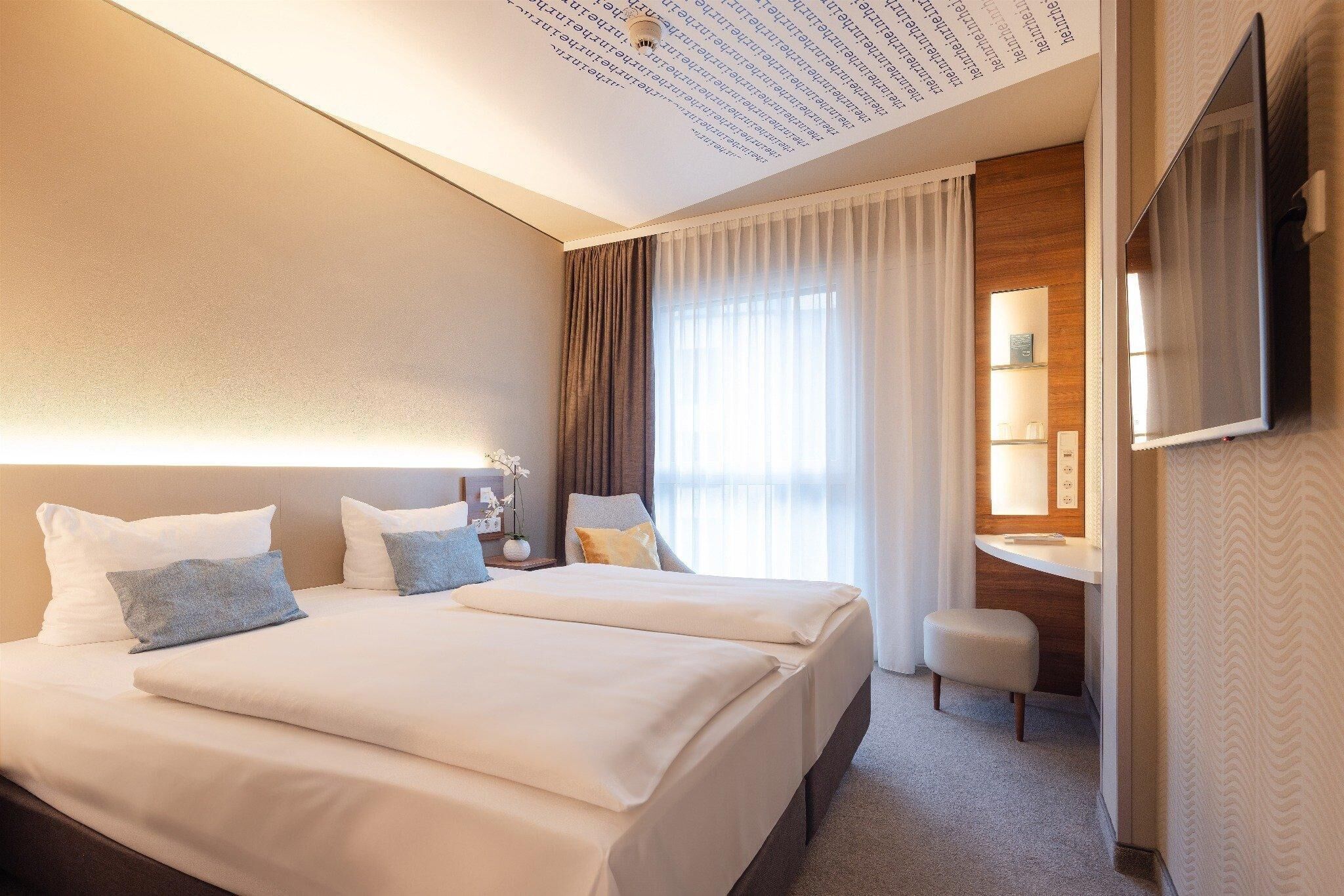 Una habitación de hotel con dos camas, un escritorio, una silla, un espejo y un televisor.
