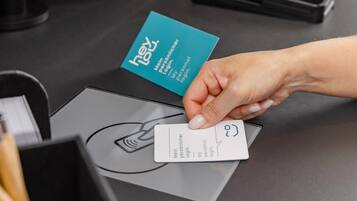 A hand holding a card with a logo and text, placed on a table with a blue card and a grey envelope.