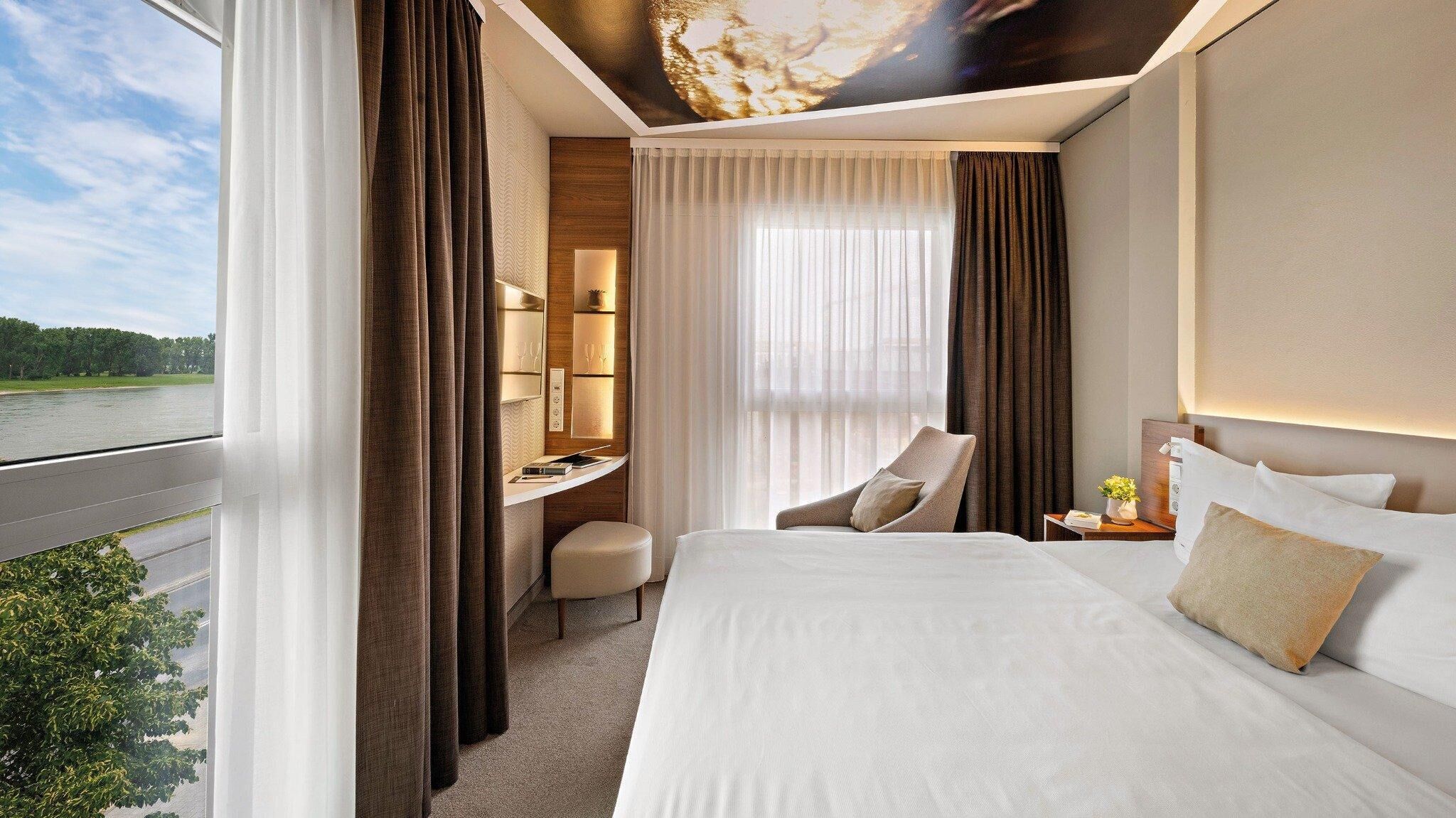 Ein Hotelzimmer mit Bett, Schreibtisch, Stuhl, Nachttisch und Blick auf ein Gewässer.