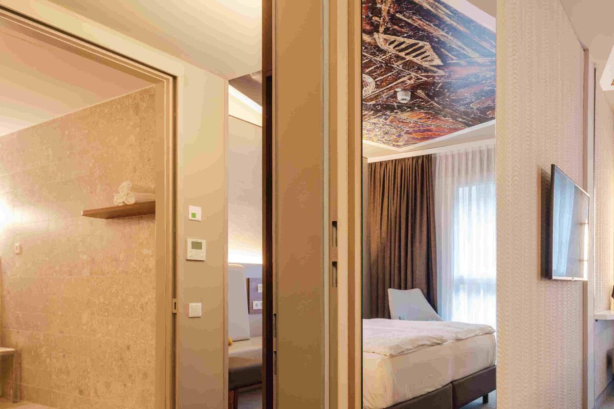 A hotel room with a bed, a TV, and a view of a cityscape through the window.