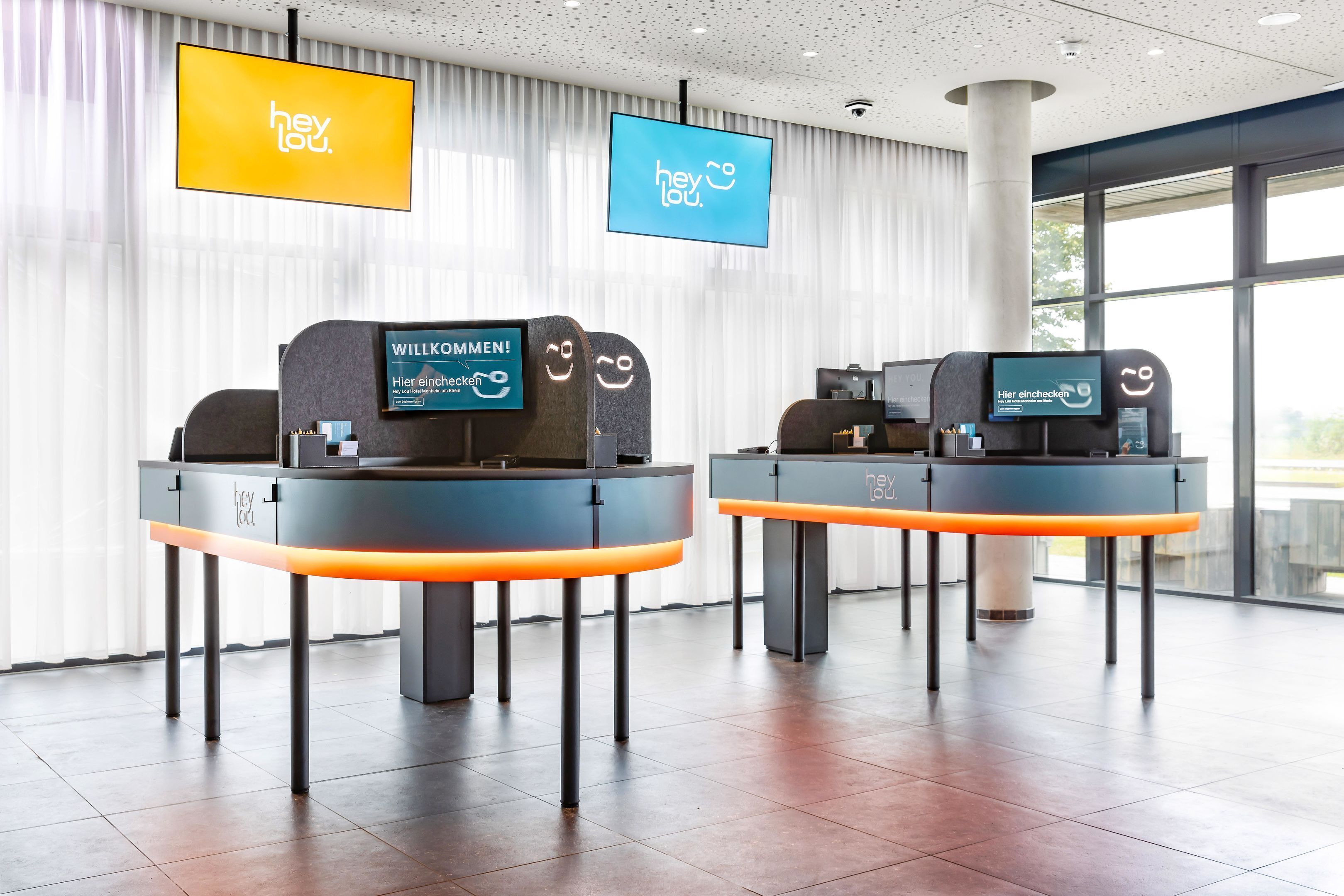 Two reception desks with digital displays, a modern interior, and large windows.