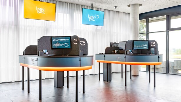 Two reception desks with digital displays, a modern interior, and large windows. - Hey Lou Hotel Monheim am Rhein (Monheim)
