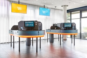 Two reception desks with digital displays, a modern interior, and large windows. - Hey Lou Hotel Monheim am Rhein (Monheim)