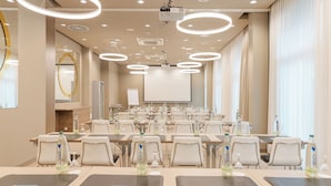 Un salón de conferencias con varias mesas, sillas y una pantalla grande al frente.