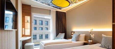 A hotel room with two beds, a desk, a chair, a TV, and a large window with a view of a building.