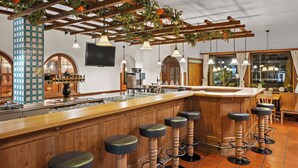 A bar area with wooden stools, a bar counter, and a coffee machine. - Styles Hotel Unterföhring (Unterfoehring)