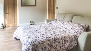 Une chambre avec une couvre-lit à motifs floraux, un plancher en bois, un canapé et une petite statue posée sur le sol.