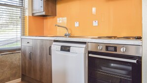 A kitchen with wooden cabinets, a dishwasher, an oven, and a window with blinds. - 2 bedroom accommodation in Commondale, near Whitby (Commondale, near Whitby)