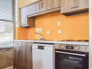 A kitchen with wooden cabinets, a dishwasher, an oven, and a window with blinds. - 2 bedroom accommodation in Commondale, near Whitby (Commondale, near Whitby)