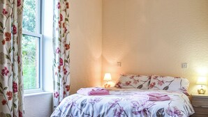 A bedroom with a bed, floral curtains, a bedside lamp, and a window. - 2 bedroom accommodation in Commondale, near Whitby (Commondale, near Whitby)