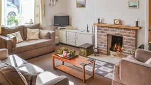 Een woonkamer met een bank, een salontafel, een open haard, een televisie en een boekenkast.
