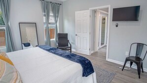Ein Schlafzimmer mit einem Bett, einem Sessel, einem Fernseher und einer Tür zu einem anderen Raum.