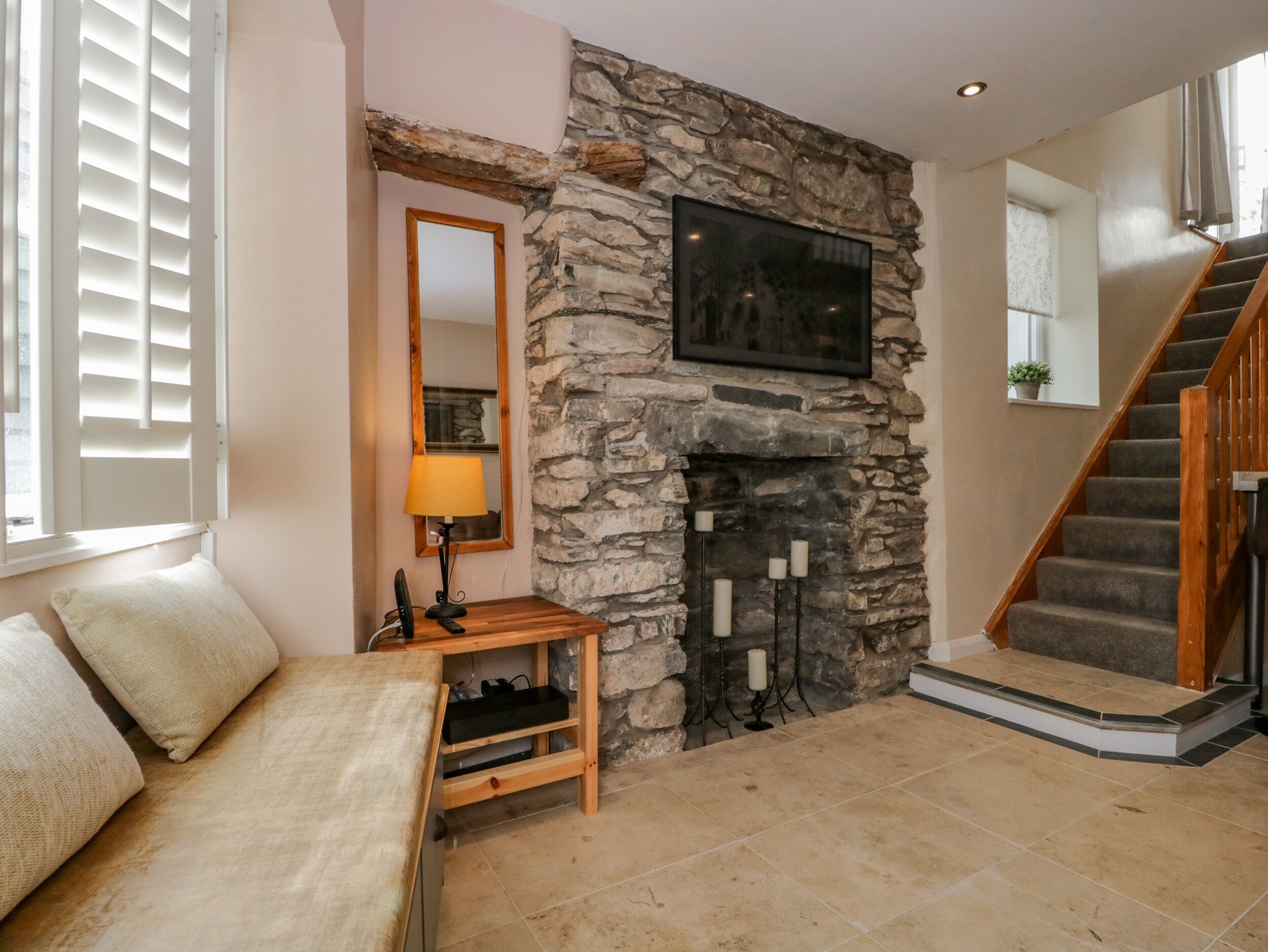 A cozy living room with a stone fireplace, a wooden bench, and a staircase.