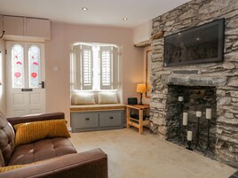 Un salón acogedor con chimenea de piedra, un sofá cómodo, un banco con cojines y una ventana con contraventanas.