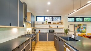 A modern kitchen with a central island, wooden flooring, and a view of the outdoors through large windows.