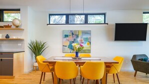 A modern dining area with a wooden table, yellow chairs, and a painting above.