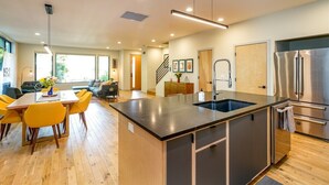 A modern kitchen with a central island, stainless steel appliances, and a dining area with yellow chairs.