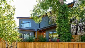 A modern two-story house with a wooden fence, large windows, and a tree in the foreground.