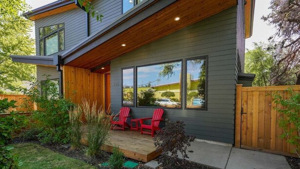 A modern two-story house with a wooden deck, large windows, and a fenced backyard.