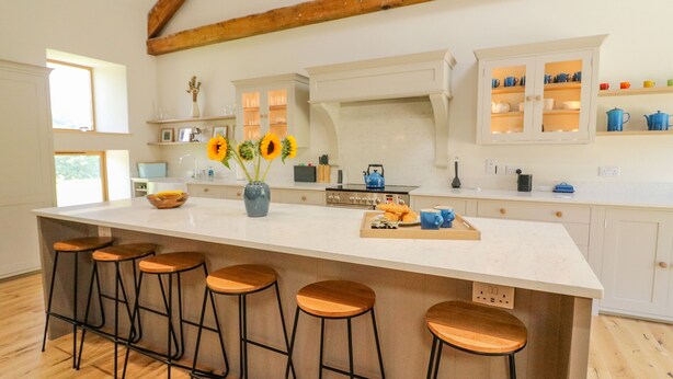 Une cuisine moderne dotée d’un grand îlot central, de tabourets de bar et de poutres en bois au plafond.