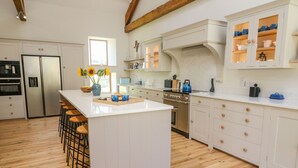 Une cuisine moderne avec des meubles blancs, un îlot central doté de tabourets, des appareils en acier inoxydable et un plancher en bois.