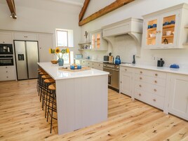 A modern kitchen with white cabinetry, a central island with stools, stainless steel appliances, and a wooden floor.