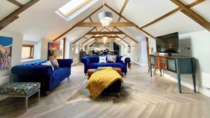 Spazioso loft con soffitti alti, travi in legno a vista, un'ampia vetrata sul tetto, un lampadario, un televisore e un'area pranzo.