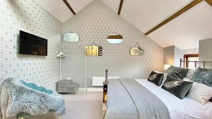 Camera da letto con soffitto spiovente, carta da parati con motivo geometrico, un letto con molti cuscini, una piccola scrivania e un televisore a parete.