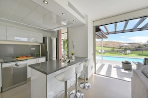 Una cucina moderna con isola centrale, elettrodomestici in acciaio inossidabile e vista su piscina e area relax all'aperto.
