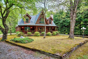 A log cabin with a wrap-around porch, surrounded by a well-maintained lawn and mature trees. - Needlepine Lodge of Sapphire Valley, Needlepine Lodge of Sapphire Valley (Jackson County)