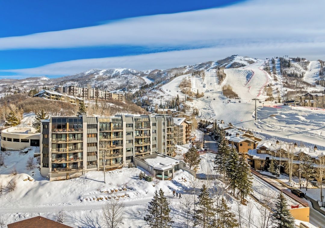 Un hôtel moderne à plusieurs étages, situé dans une région montagneuse enneigée, avec des pistes de ski visibles au loin.