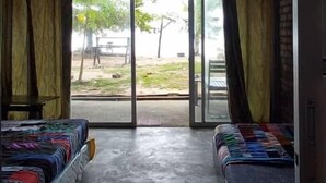 A room with two beds, a concrete floor, and a view of an outdoor area with trees and a table. - Hotel O Naga Puri Beach Retreat (Kuala Penyu)