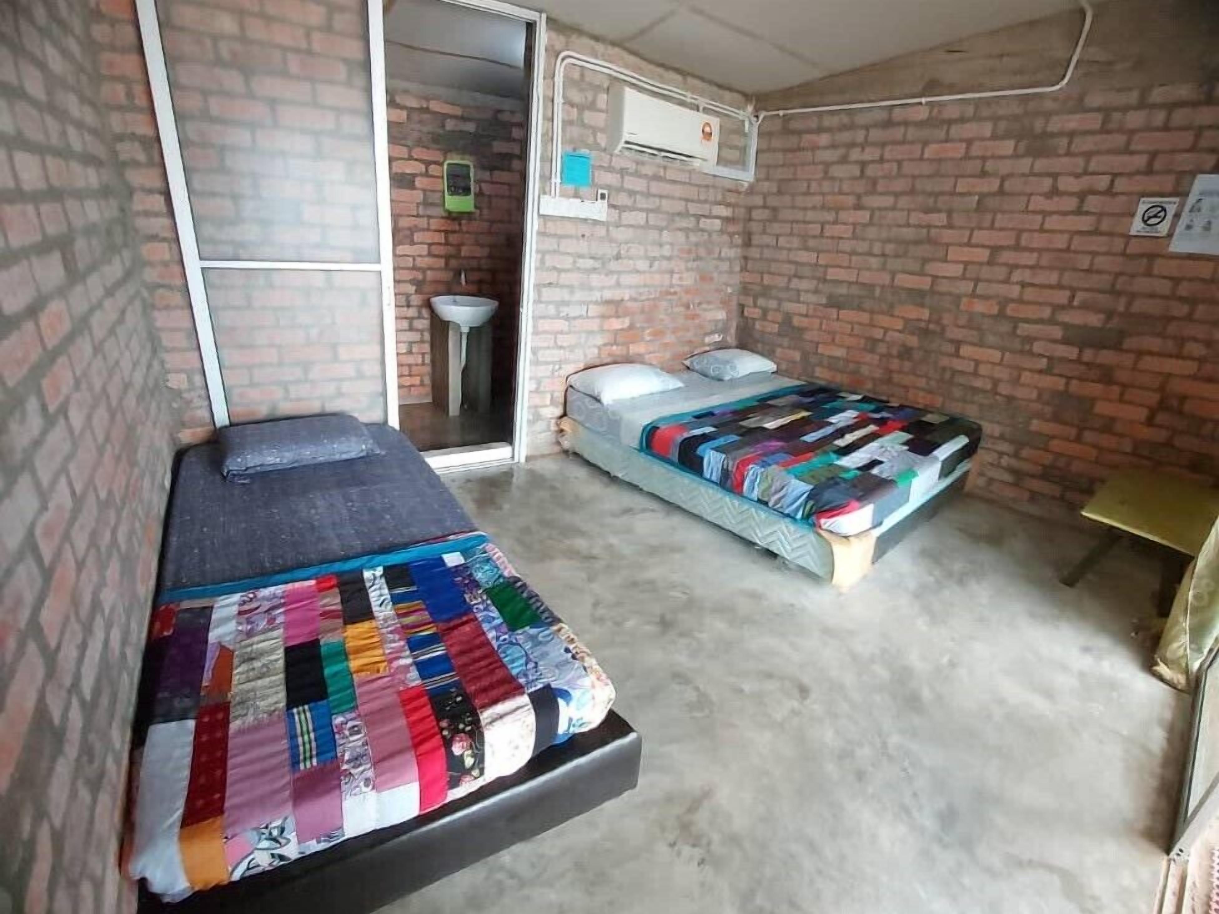 Una habitació amb dos llits, una taula petita i una paret de maó.