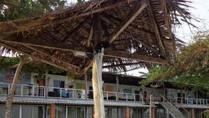 A beachside building with a thatched roof, a staircase leading to a balcony, and a sandy ground. - Hotel O Naga Puri Beach Retreat (Kuala Penyu)