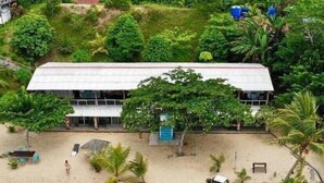 A building with a flat roof and large windows, surrounded by dense greenery and a sandy area with a few people and a small vehicle. - Hotel O Naga Puri Beach Retreat (Kuala Penyu)