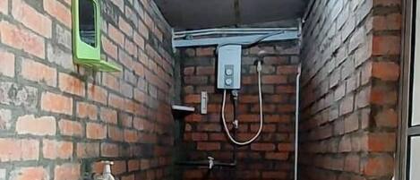 A narrow hallway with a white sink and a green mirror on the left, brick walls, and a shower area with a hose on the right.