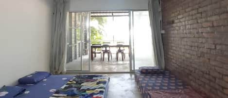A room with two beds, a brick wall, a sliding glass door leading to an outdoor area with a table and chairs.